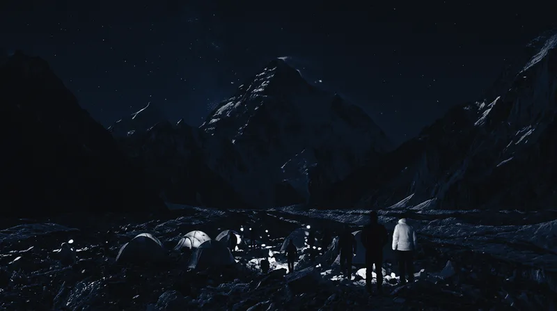 Tents glowing at K2 Base Camp at night, with the mountain behind