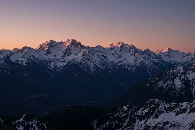 Snow peaks lit rose-gold above a valley already in blue shadow.