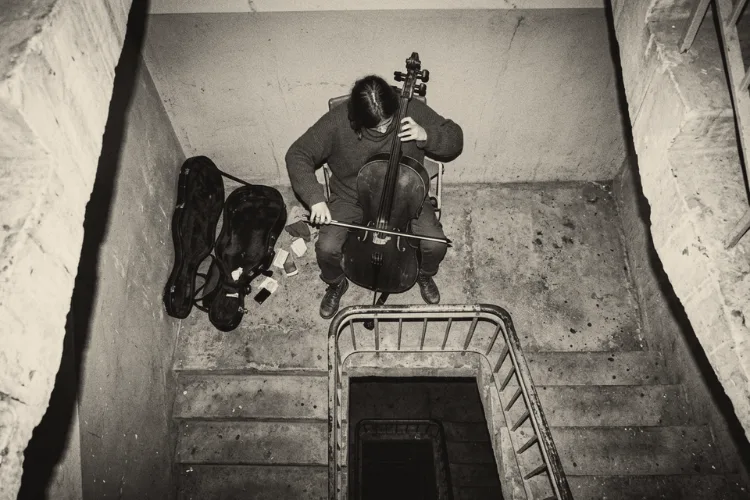 A cellist seen from above, playing alone on a stairwell landing